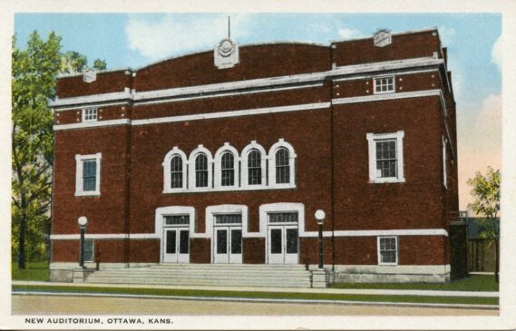 A large brick building with an arched roof and stone accents. Stairs lead to three pairs of doors. 