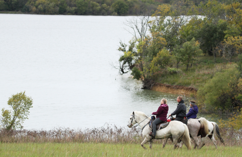 People riding horses near the shore of a lake.